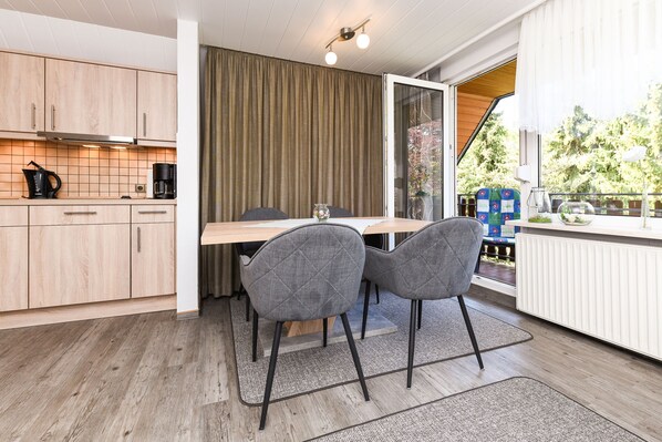 A modern kitchen with wooden cabinets, a dining table with two chairs, and a view of the outdoors through a sliding glass door.