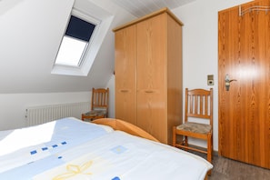 Ein Schlafzimmer mit einem Bett, einem Holzschrank, einem Stuhl, einem Fenster und einer Heizung.
