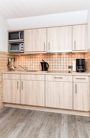 A modern kitchen with wooden cabinets, a microwave, a coffee maker, and a sink.