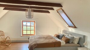 A bedroom with a sloped ceiling, a bed, a chair, and a window. - Vacation accommodation "Verwalterhaus" with view of the horse pasture -Gut Wittmoldt- (Wittmoldt)