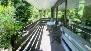 Un espace extérieur abrité, doté d’un banc et de tables en bois, et entouré de verdure.
