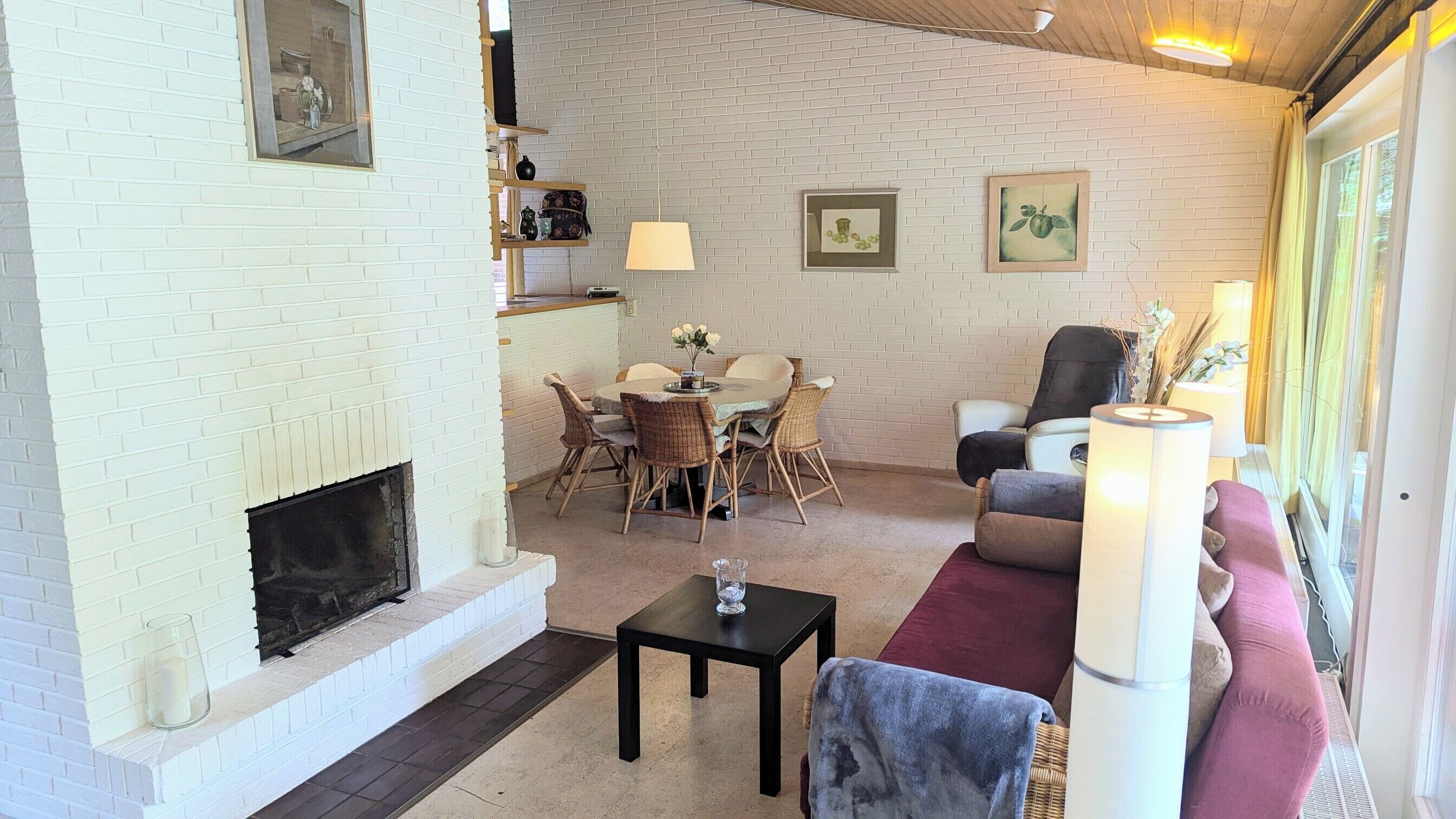 Un salon chaleureux avec une cheminée, un coin repas avec des chaises en osier, un canapé et une table basse.