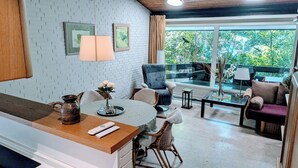 Une cuisine moderne avec un coin repas, un balcon offrant une vue sur la verdure et un espace salon avec un canapé et des fauteuils.