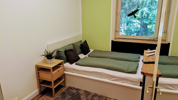 A small, cozy room with a bed, a nightstand, a window, and a view of a bird flying outside. - Relaxation, peace, and fresh air in the heart of nature on the Heidschnucken hiking trail (Egestorf)
