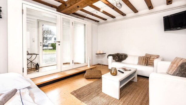 A modern living room with a white sofa, a coffee table, and a large glass door leading to an outdoor area.