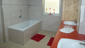 Een badkamer met een bad, een wastafel en een raam met bloemen.