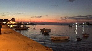 A waterfront scene with boats docked along the pier, a calm body of water, and a city skyline in the background. - unique historical STONE TOWER DIRECTLY BY THE SEA! carefully restored (Umag)