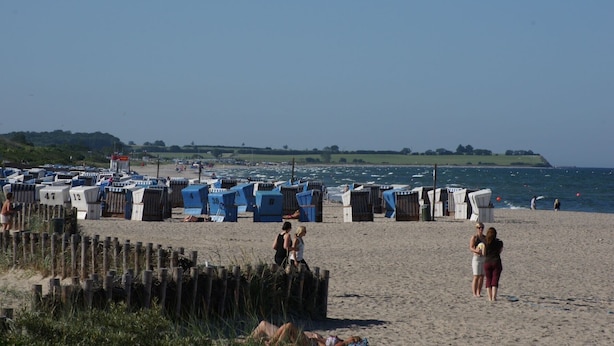 A beach with numerous blue and white beach huts, some with numbers on them, and a few people walking around. - Log house with large garden - WiFi included - only 5 minutes to the beach  (Ostseebad Damp)