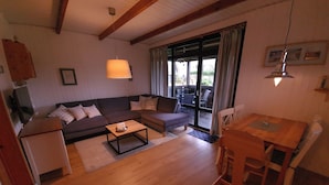 A cozy living room with a sofa, coffee table, and a dining area with a table and chairs. - Log house with large garden - WiFi included - only 5 minutes to the beach  (Ostseebad Damp)