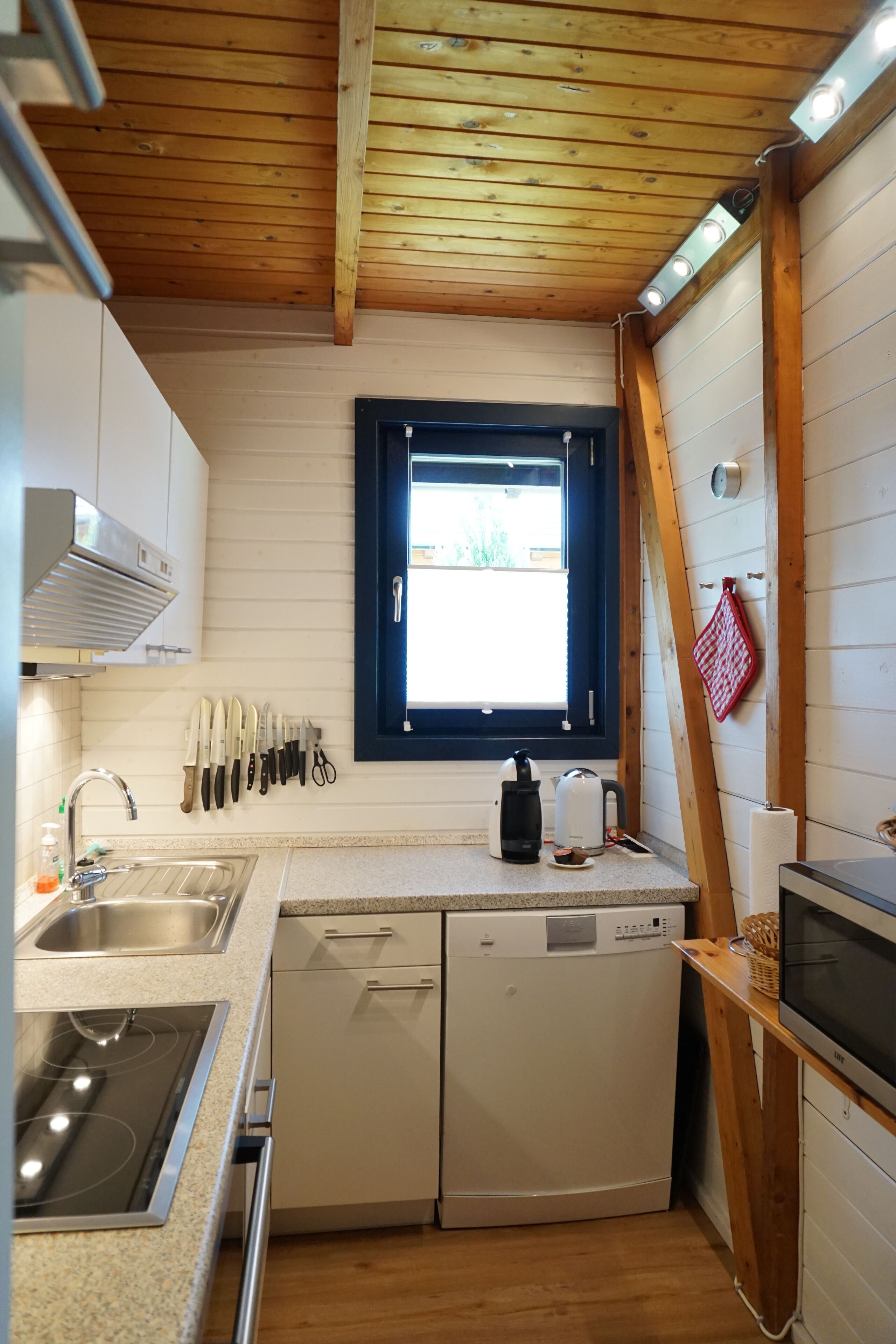 Eine kompakte Küche mit Holzboden, einem Fenster, einer Spüle, einem Geschirrspüler und einer Mikrowelle.