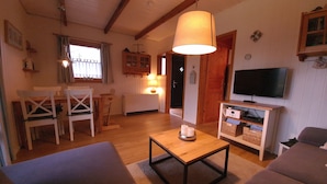 A cozy living room with a wooden table, a sofa, a television, and a dining area with chairs and a cabinet. - Log house with large garden - WiFi included - only 5 minutes to the beach  (Ostseebad Damp)