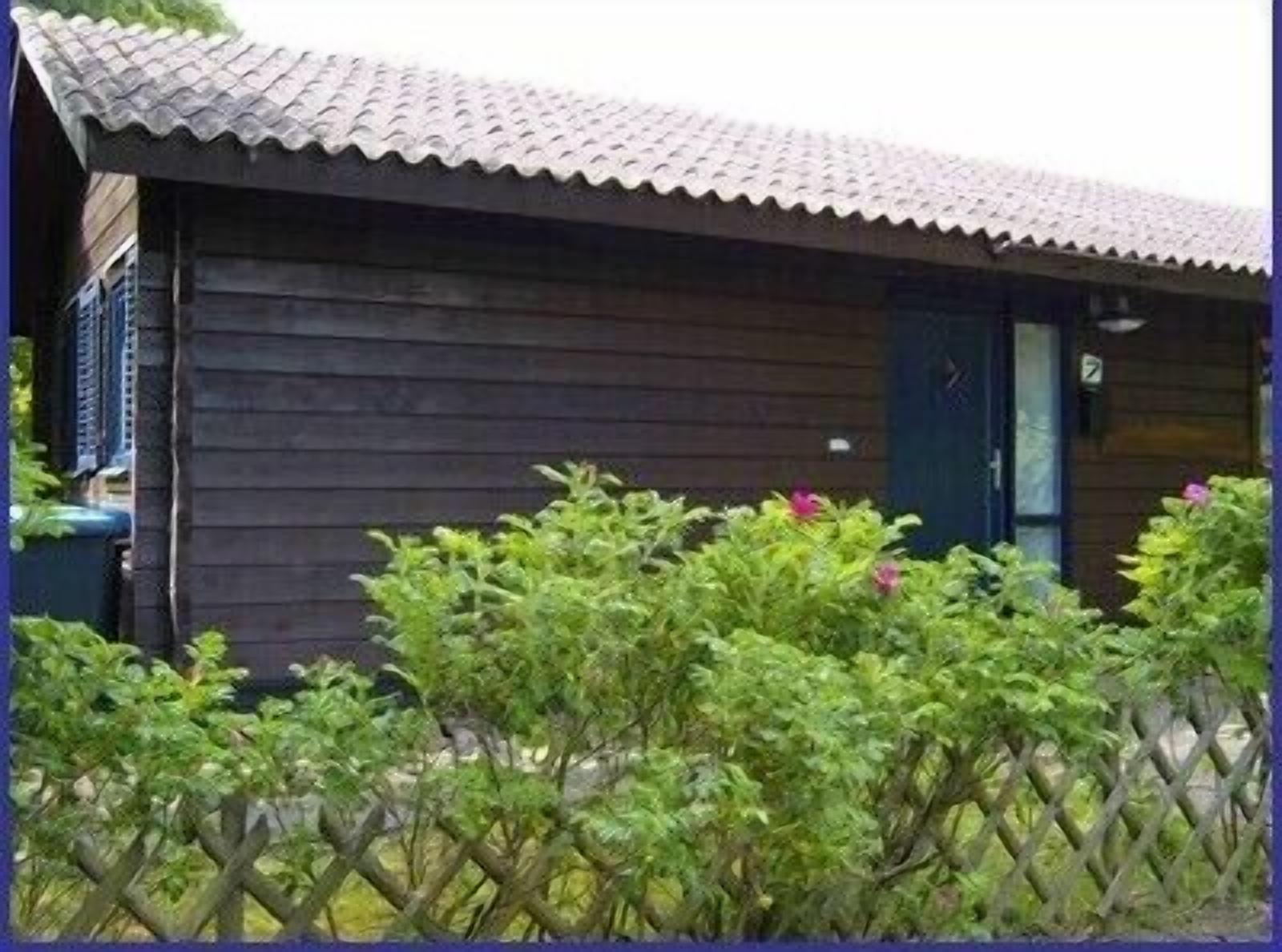 A wooden cabin with a tiled roof, surrounded by a wooden fence and lush greenery.
