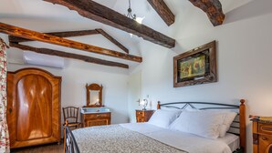 Un dormitorio con cama y armario de madera, una silla, una mesita de noche y un cuadro en la pared.