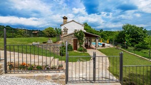 Una casa de piedra con piscina, rodeada por un jardín vallado y un cielo despejado.