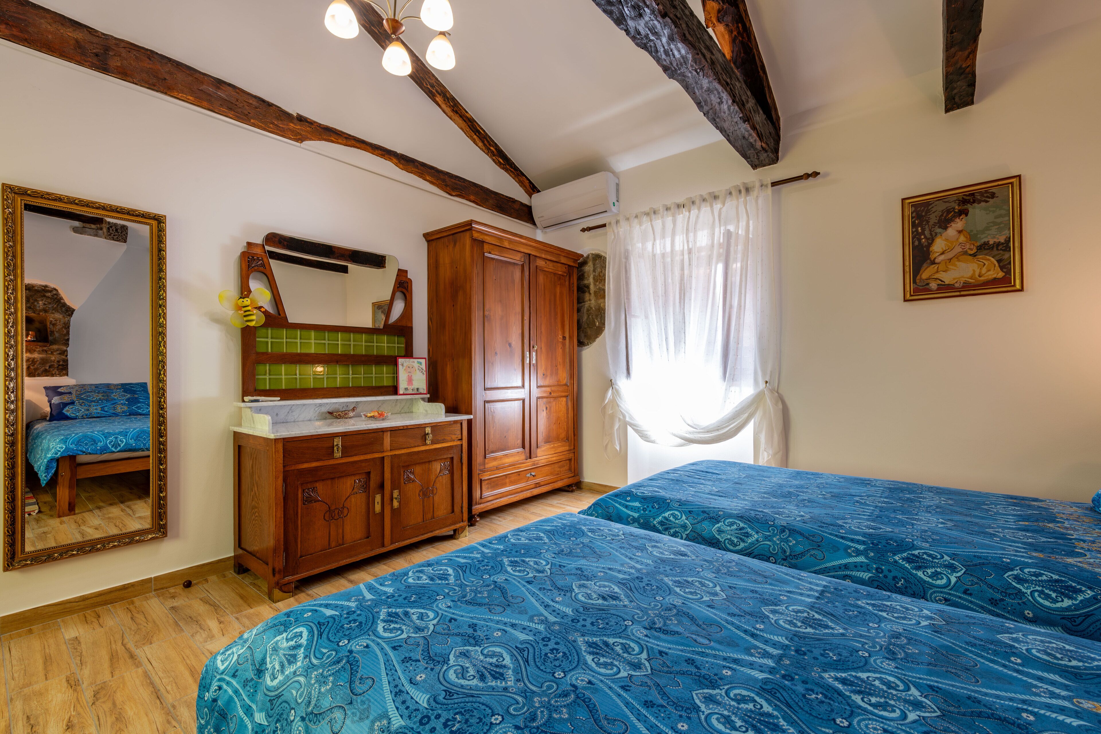 A bedroom with two beds, wooden furniture, a mirror, and a painting.