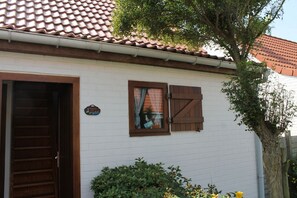 Un edificio blanco con tejado de tejas, puerta de madera y ventana con contraventanas.