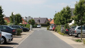 A residential street with parked cars and bicycles, houses with red roofs, and a clear sky. - Bright vacation home for up to 6 people with fireplace, garden, parking and WiFi in De Haan (De Haan)