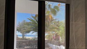 A view through a window with a beach and palm trees in the background. - Beautiful apartment in the nature reserve "Risco del Paso" ideal for nature lovers (Costa Calma)