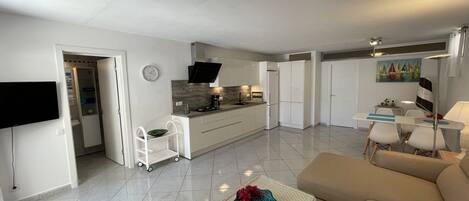 Un appartement moderne comprenant une cuisine, un coin repas et un salon. Il est équipé d’un téléviseur à écran plat, d’une table à manger avec des chaises, d’un canapé et d’une machine à café.