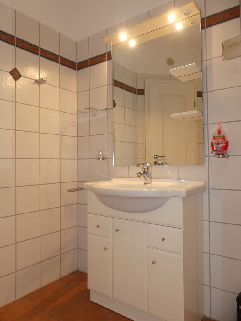 Une salle de bain avec un lavabo blanc, un miroir et des murs carrelés.