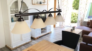Un comedor con mesa y sillas de madera, un armario blanco con puertas de cristal y una lámpara de techo.