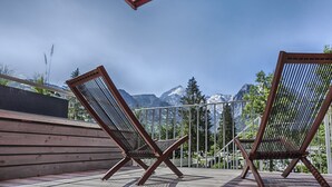 Zwei Holz-Loungesessel mit Metallgestell auf einer Terrasse mit Blick auf Berge und Bäume.