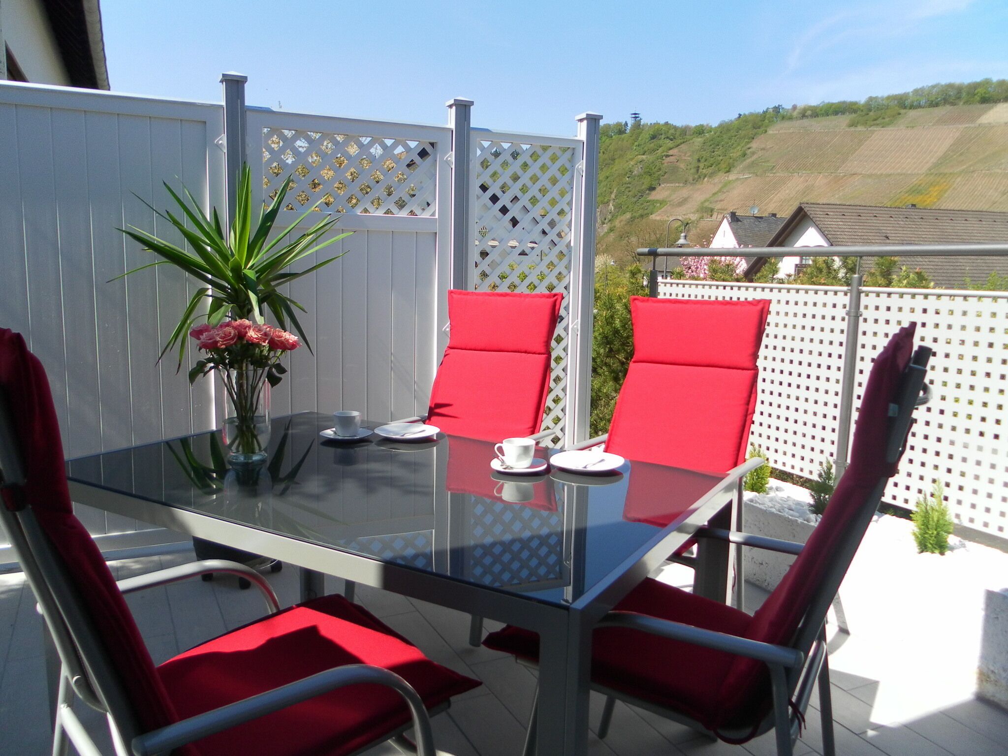 Eine Terrasse im Freien mit einem Glastisch, roten Stühlen und einem weißen Zaun.