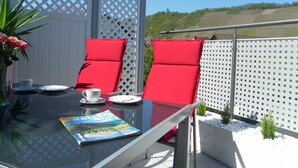 A glass-top table with two red cushioned chairs, a white table runner, a magazine, and a small plant. - Welcome Holiday home Schmitz No. 2, for 2 to 4 people.  with Wi-Fi (Pünderich/Mosel)