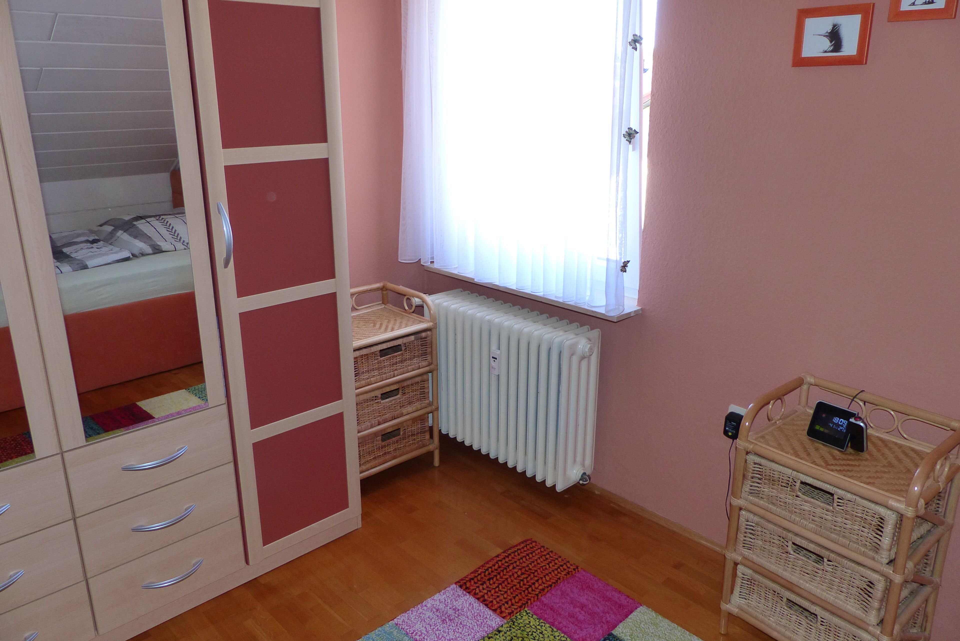 Een slaapkamer met een bed, een kledingkast, een radiator en een klein tafeltje met een klok.