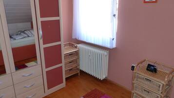 Een slaapkamer met een bed, een kledingkast, een radiator en een klein tafeltje met een klok.