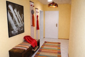 A hallway with a bench, a door, a colorful rug, and a wall-mounted light fixture. - Apartment with a View – modern living above the rooftops (Wörth am Rhein)