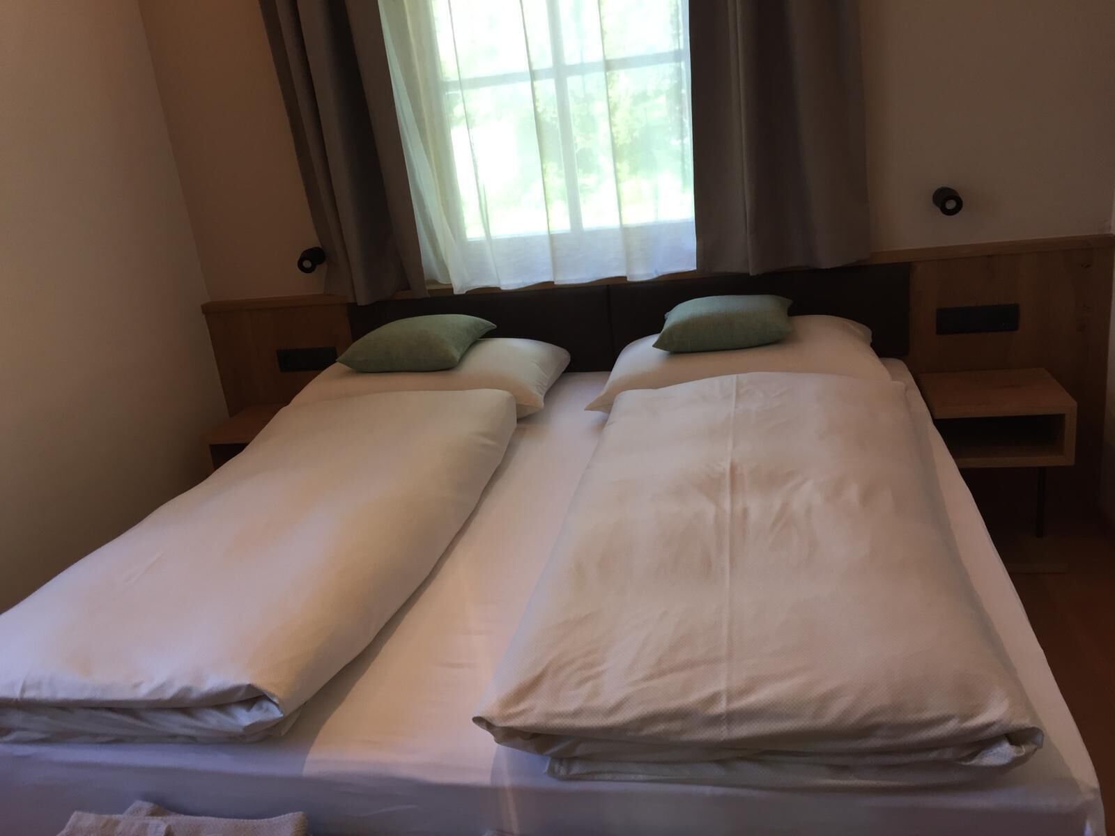 Un llit doble amb dues almoines, una petita taula de nit i una finestra amb cortines.