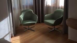 Une pièce avec deux fauteuils verts, un plancher en bois et une grande fenêtre avec des rideaux.