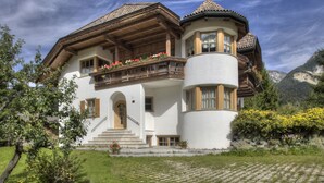 Un chalet traditionnel doté d’un balcon en bois, d’une tourelle et d’un escalier en pierre menant à l’entrée.