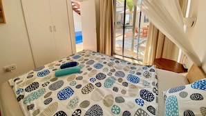 Una habitación de hotel con cama, armario, ventana con cortinas y vista al exterior.