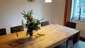 Een eetruimte met een houten tafel, stoelen, een kleine kerstboom en hanglampen.