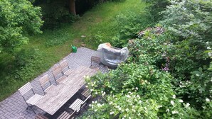 Een houten terras met een tafel en banken, omgeven door weelderige begroeiing en bomen.