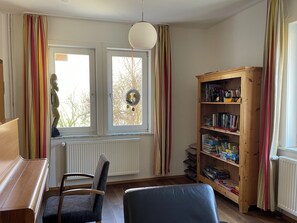 A room with a wooden bookshelf, a window with curtains, a radiator, and a chair.