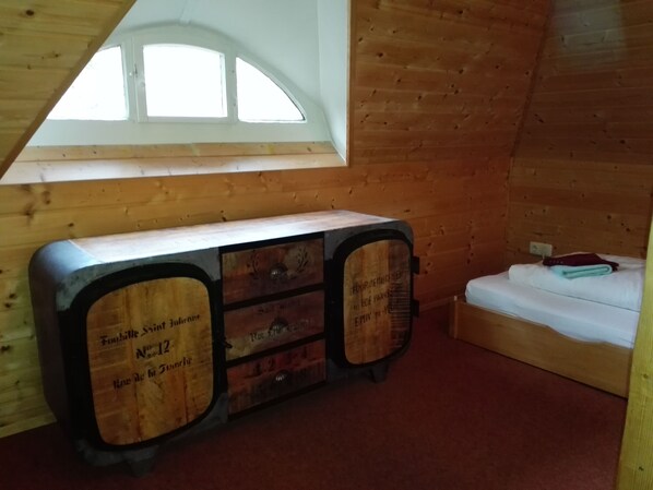 Una cabaña de madera con cama en altillo, una ventana pequeña y un aparador de madera con etiquetas.