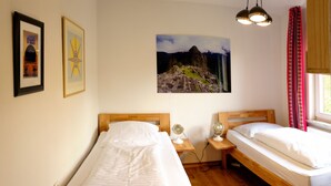 Een slaapkamer met twee bedden, een houten hoofdbord, een nachtkastje met een lamp en een aan de muur hangend schilderij.