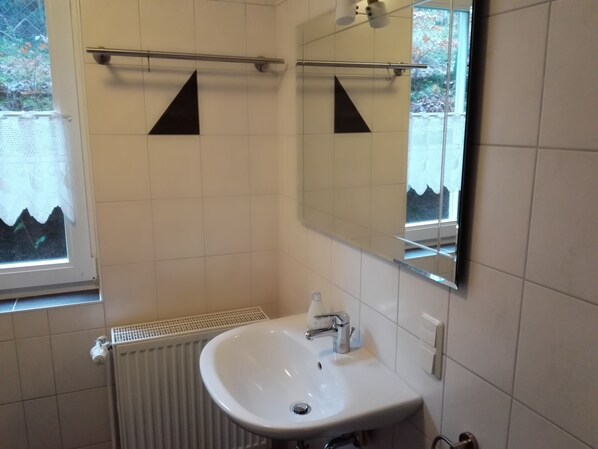 A bathroom with a white sink, a mirror, and a radiator. There are black triangular decorations on the wall.
