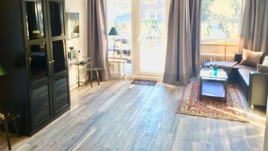 A living room with a dark wooden cabinet, a sofa, a coffee table, and a view through large windows. - 1st beach row Kaiserallee incl. WLAN, 2 bicycles, beach chair package possible (Lübeck)