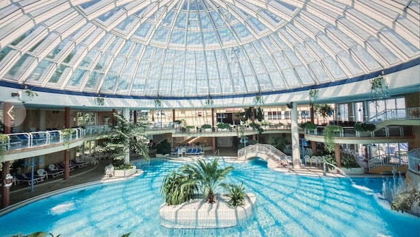 A large indoor swimming pool with a glass dome ceiling, multiple levels with balconies, and various seating areas. - 1st beach row Kaiserallee incl. WLAN, 2 bicycles, beach chair package possible (Lübeck)