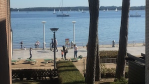A waterfront promenade with people walking, benches, and sailboats in the distance. - 1st beach row Kaiserallee incl. WLAN, 2 bicycles, beach chair package possible (Lübeck)