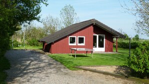 A red building with a gravel path leading to a table and chairs outside.