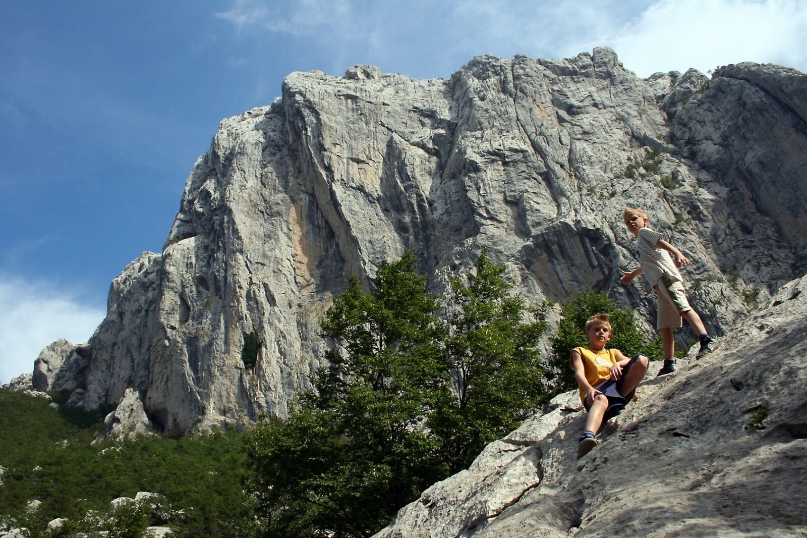 A rocky landscape with two people climbing a steep rock face.
