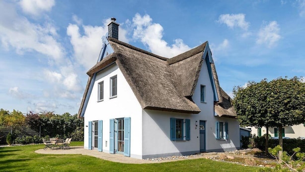 Une maison blanche avec des volets bleus et un toit de chaume.