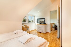 Une chambre avec deux lits, une télévision, une commode et une fenêtre.