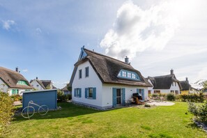 Une maison traditionnelle avec un toit de chaume, une façade blanche et des volets bleus.