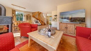 Un salon spacieux avec une cheminée, des canapés rouges, une table basse en bois et un grand téléviseur.